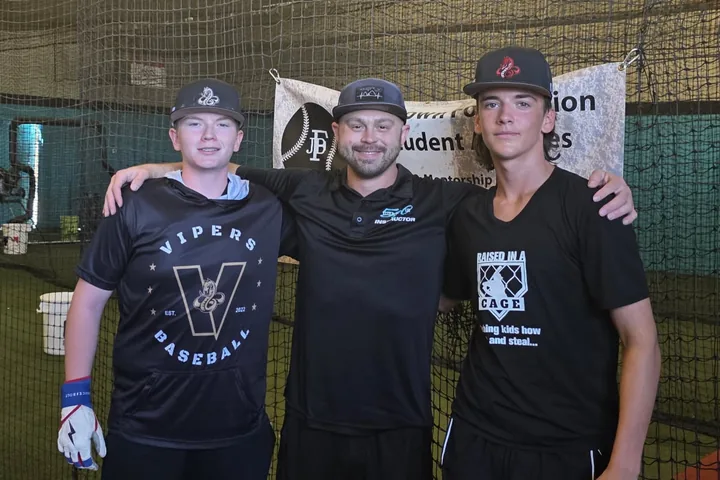 Sean Ramalho with two of his players, arms around shoulders, inside a batting cage facility