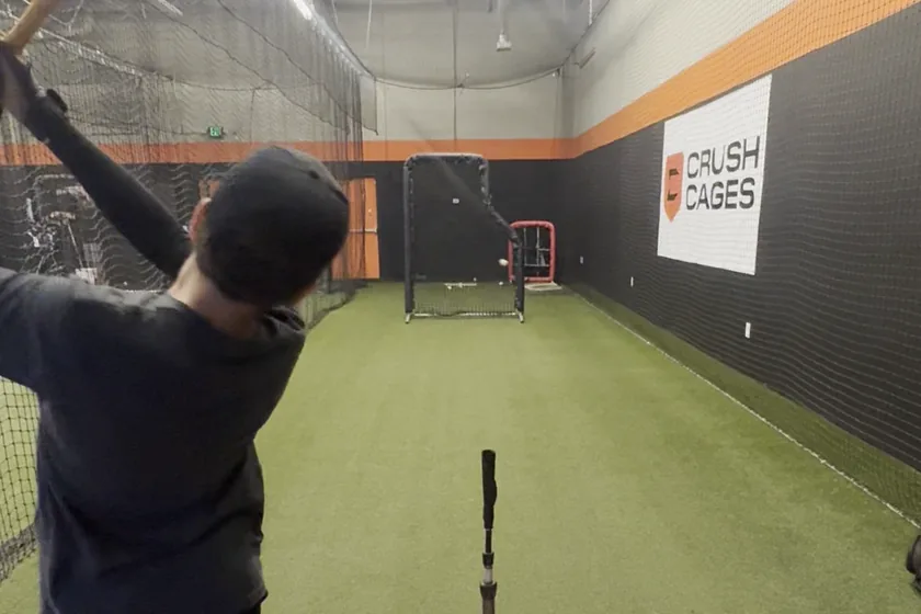A young hitter at the finish of his swing, bat high, looking down an empty cage