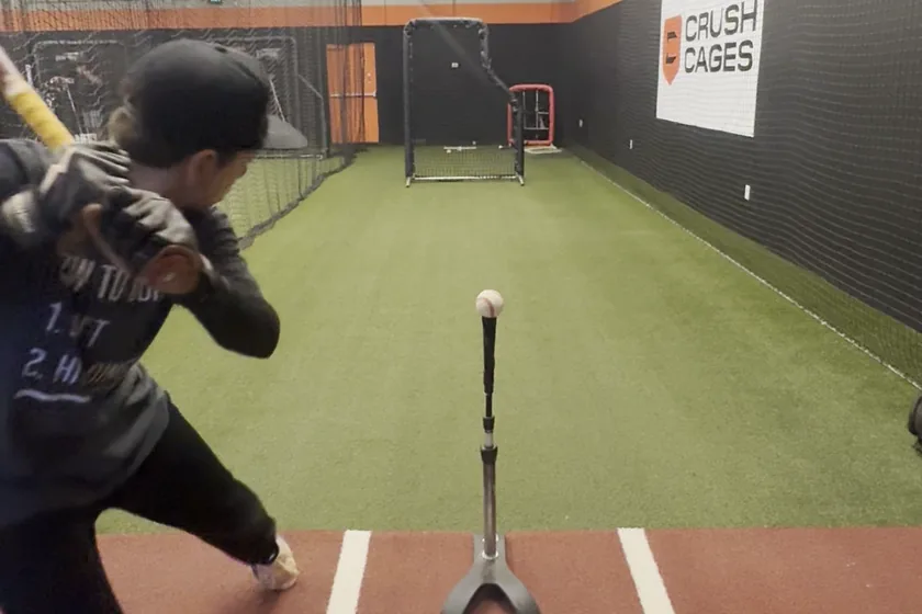 A young hitter loaded up with the bat back, a ball waiting on the tee in front of him